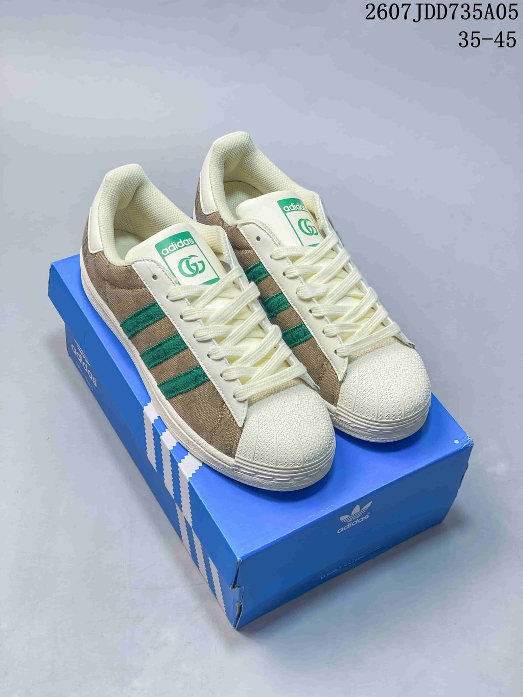 Pair of beige and green Adidas Superstar-style sneakers displayed on a blue Adidas shoebox; overlay text shows style code 2607JDD735A05 and size range 35–45.