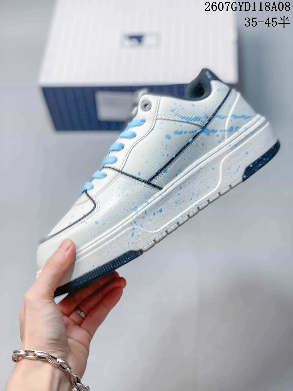 Side profile of the white sneaker showing blue splatter accents, stitched panels, a layered sole and dark trim.