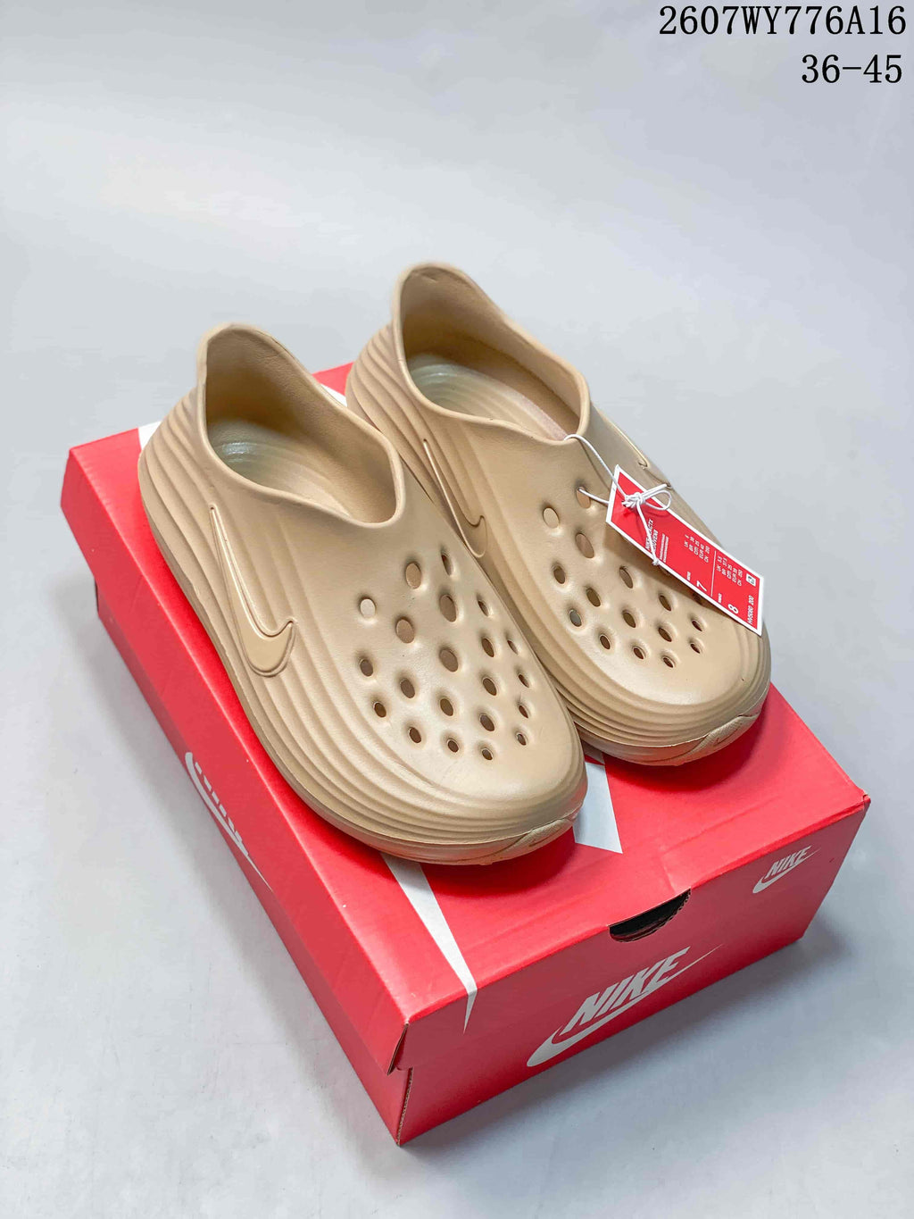 Pair of tan Nike ReactX Rejuven8 clogs displayed on a red Nike shoe box; style code 2607WY776A16 and size range 36–45 are visible.