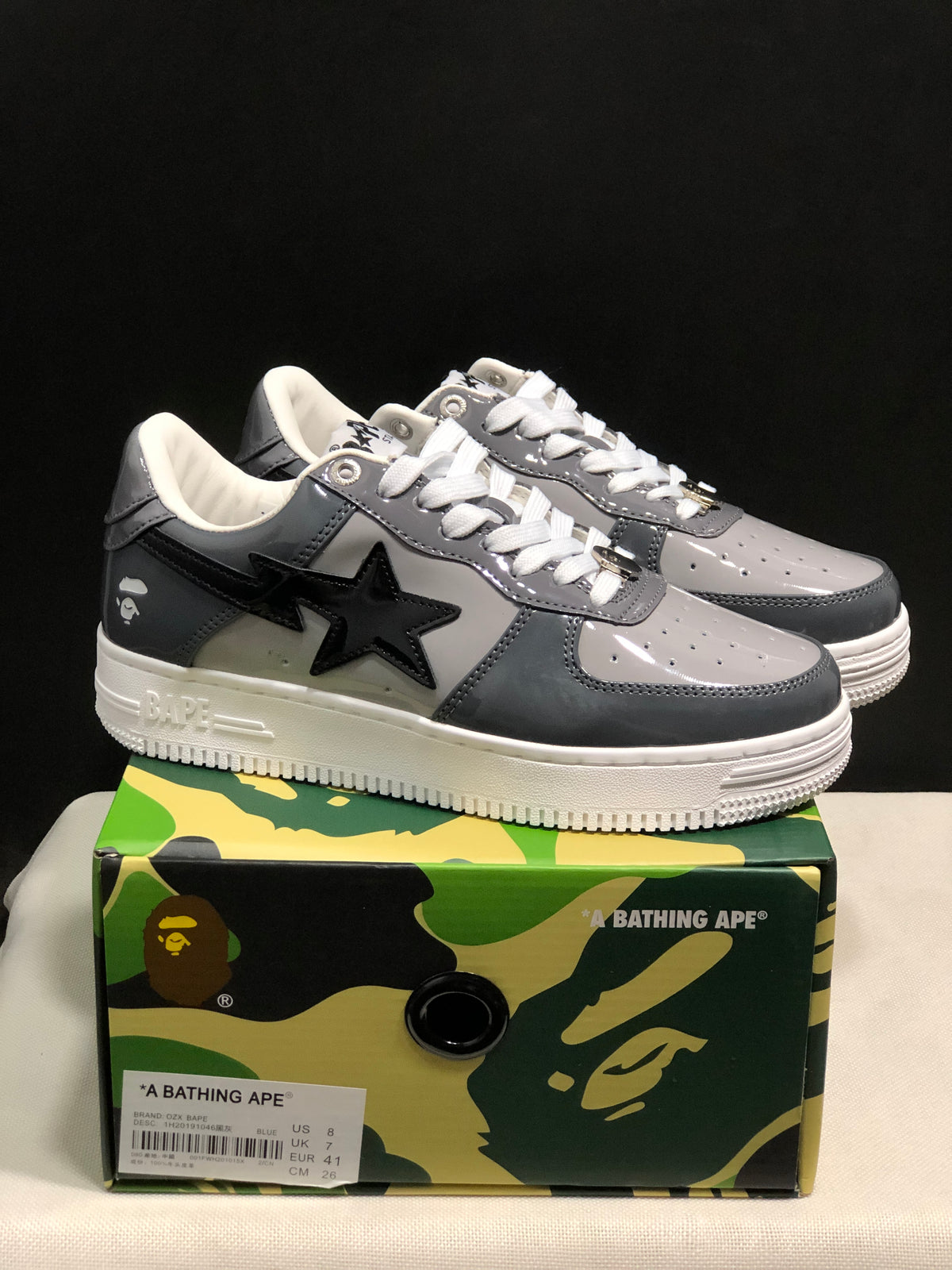 Pair of dark gray and black Bapesta low-top sneakers displayed on a BAPE-branded camouflage shoe box.