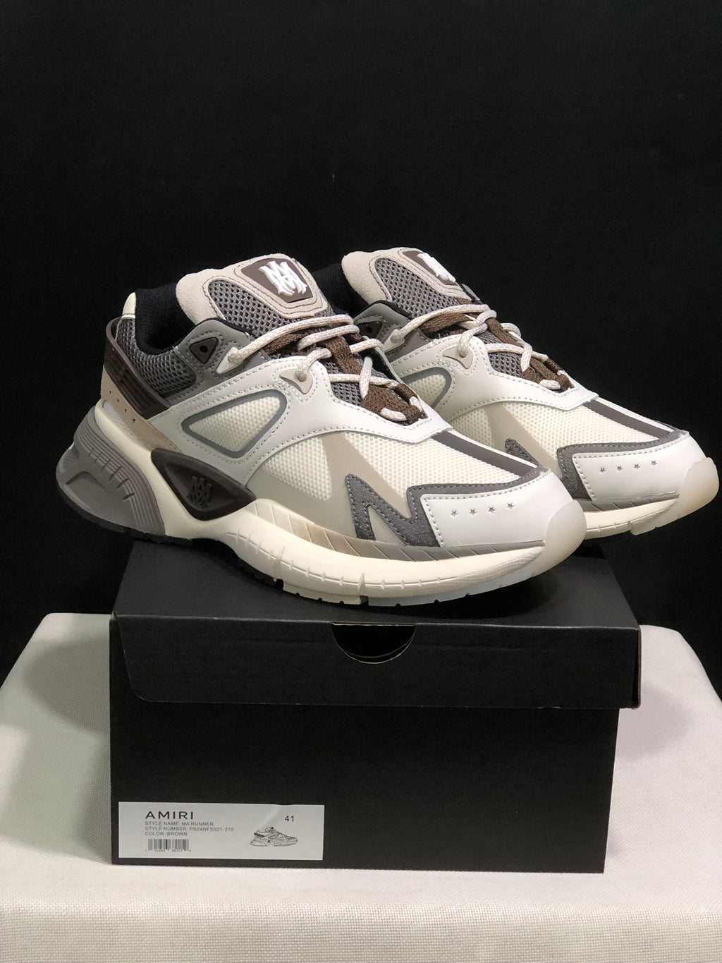 Front three-quarter view of the pair displayed on a black AMIRI shoe box.