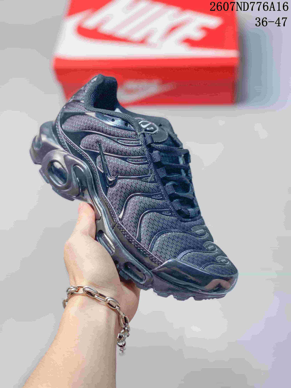Angled side view of a black Nike Air Max Plus sneaker showing the layered upper, wavy overlays, side branding, and sculpted cushioning sole.
