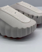 Close-up of the perforated upper strap and scalloped front edge on the light pink and white slide sandal.