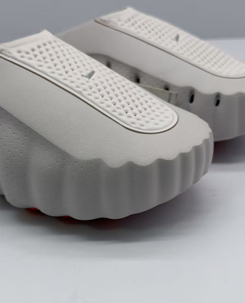 Close-up of the perforated upper strap and scalloped front edge on the light pink and white slide sandal.