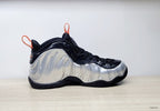 Side profile of a high-top sneaker with a silver molded-looking panel, black upper, and orange pull tab