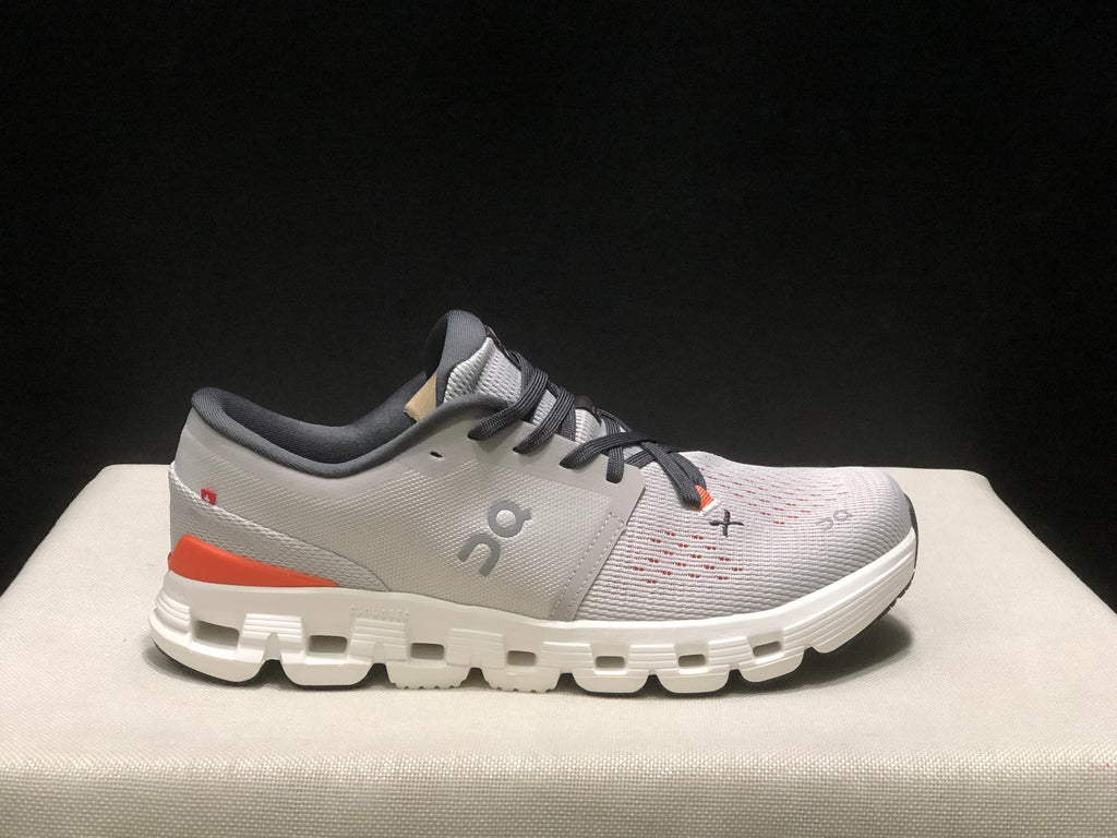 Side profile of one shoe showing the silver upper, orange heel accent, dark collar, and white outsole.