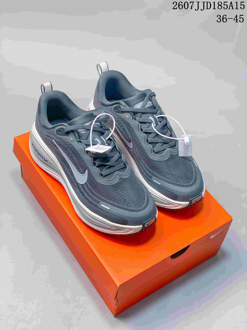 Pair of dark gray and white Nike Vomero Plus Run sneakers displayed on an orange shoe box.