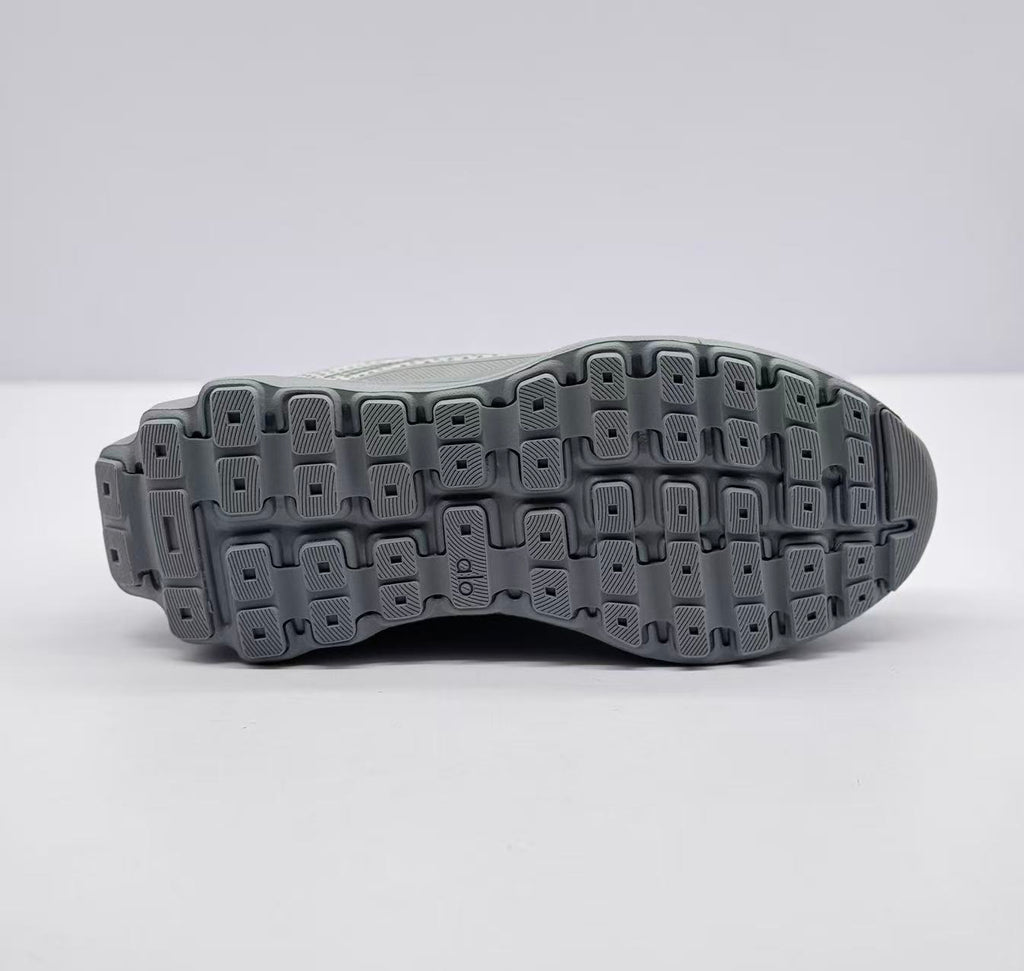 Underside view showing the segmented gray outsole with a lugged tread pattern and Alo branding.