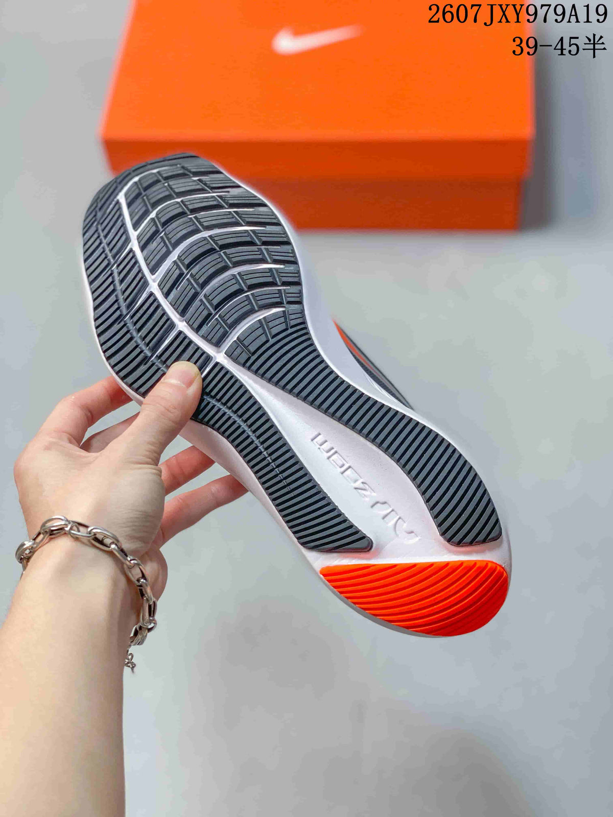 Underside view of the Nike running shoe showing the patterned outsole tread and orange heel section; image text shows style code 2607JXY979A19 and size range 39–45.