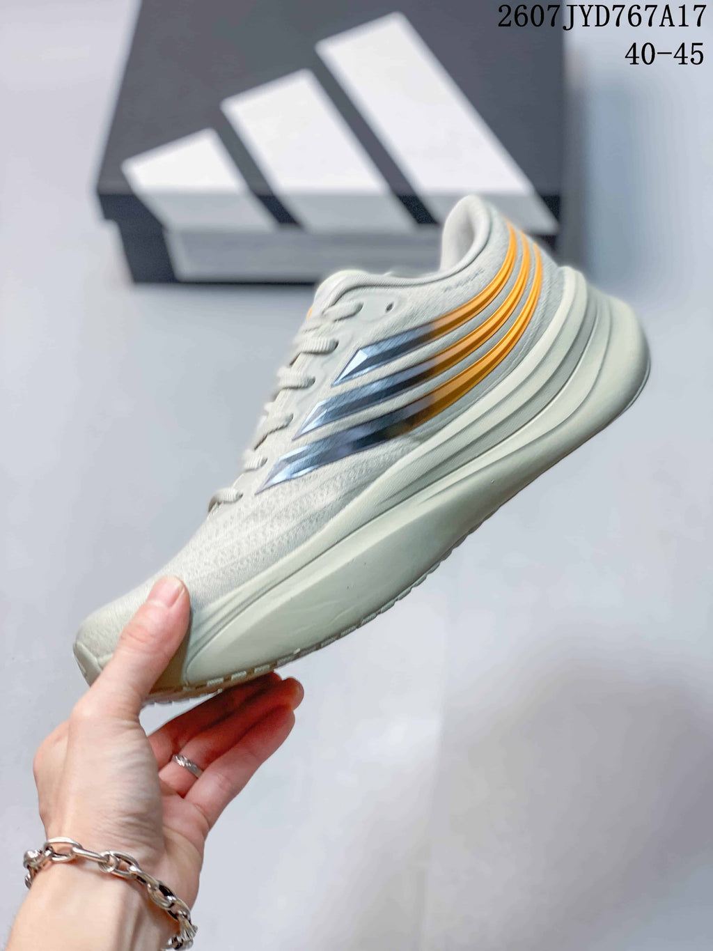 Side profile of the sneaker showing the light gray upper, navy and orange side detailing, lace closure, and thick midsole.