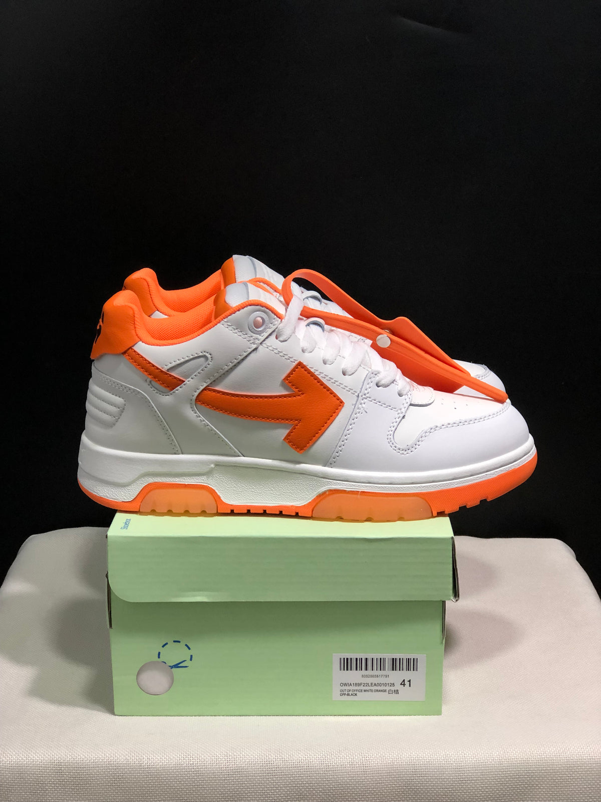 Side view of the white low-top sneakers showing orange arrow accents, orange collar lining, and orange outsole sections.