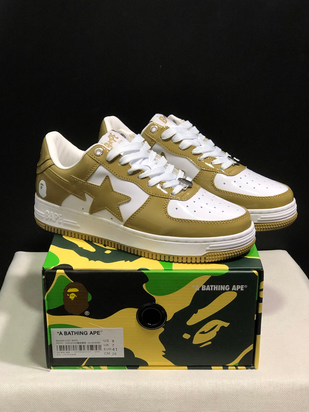 Pair of olive and white BAPE STA low-top sneakers displayed on a camouflage-patterned shoebox; the box label shows EU 41, US 8, UK 7, and CM 26.