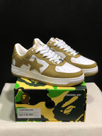 Pair of olive and white BAPE STA low-top sneakers displayed on a camouflage-patterned shoebox; the box label shows EU 41, US 8, UK 7, and CM 26.