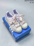 Pair of white Adidas Superstar sneakers with lilac accents, pink ribbon laces, colorful beads, and a blue Adidas shoebox.