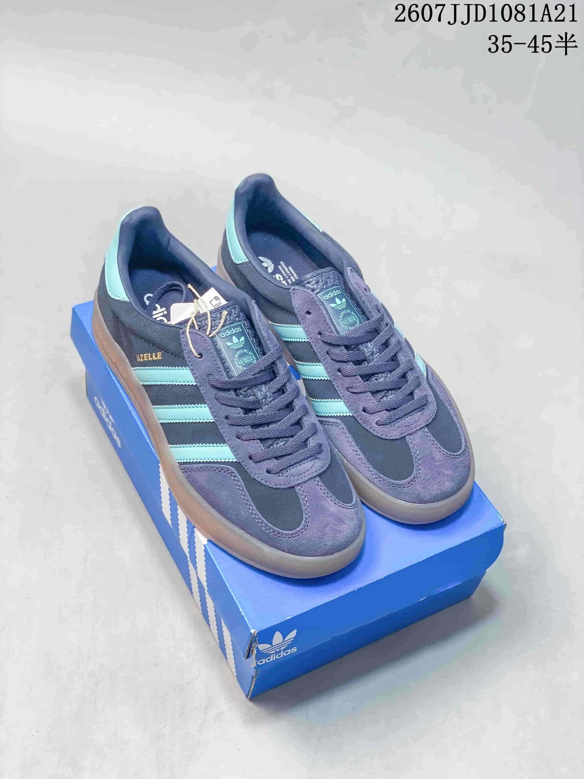 Pair of adidas Gazelle Indoor sneakers in navy and purple-blue with turquoise stripes, displayed on a blue adidas shoebox.