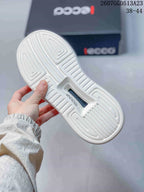 Close view of the white patterned outsole of a beige ECCO sneaker, with ECCO branding visible on the sole and box.