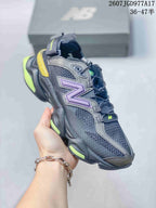 Angled side view of the black, purple and fluorescent yellow New Balance 9060 sneaker showing the mesh upper, layered overlays and thick sculpted sole.