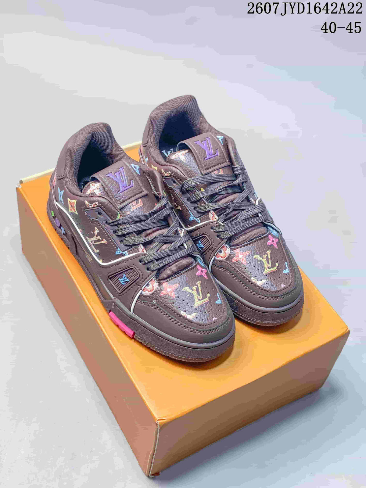 Pair of dark brown Louis Vuitton Trainer low-top sneakers with multicolor motifs displayed on an orange box; image text shows 2607 TYD1642A22 and 40–45.