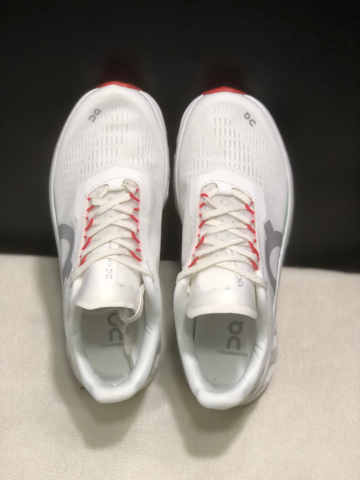 Top view of the pair showing the white perforated-looking upper, lace system, gray On logos, and red lace accents.