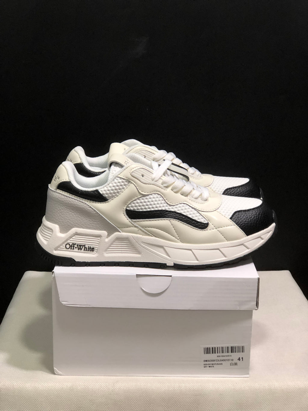 Side view of white and black low-top sneakers showing the layered upper, black accents, and branded side detail.