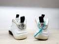 Rear view of white Nike Air Foamposite One sneakers with beige and gray marbled heel accents and black pull tabs.