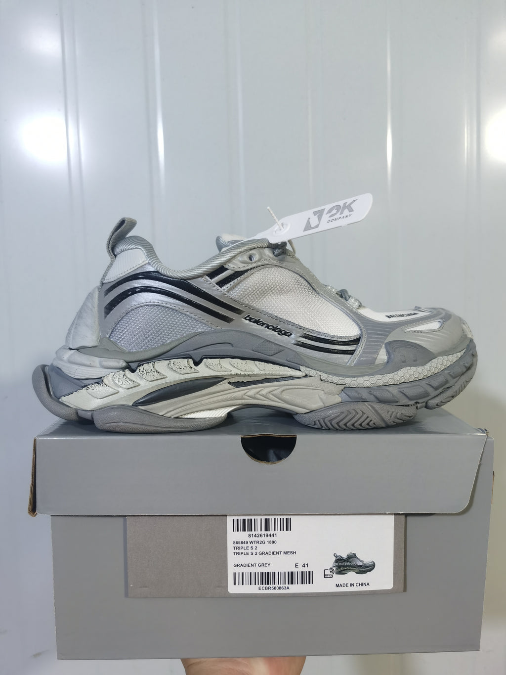 Side view of the gradient grey sneakers resting on the shoe box, with the product label visible beneath.