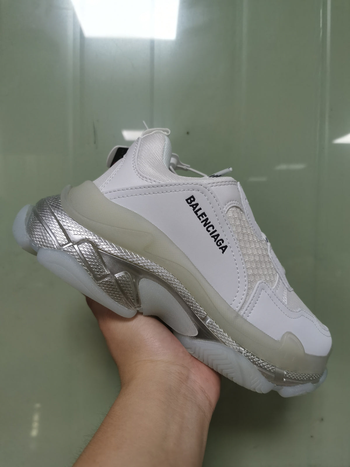 Side view of the white Balenciaga sneaker showing layered panels, black side branding, and the sculpted iridescent sole.