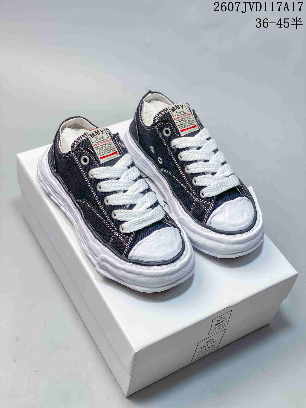 Black MMY low-top canvas sneakers with white laces and a sculpted white sole displayed on a shoebox.