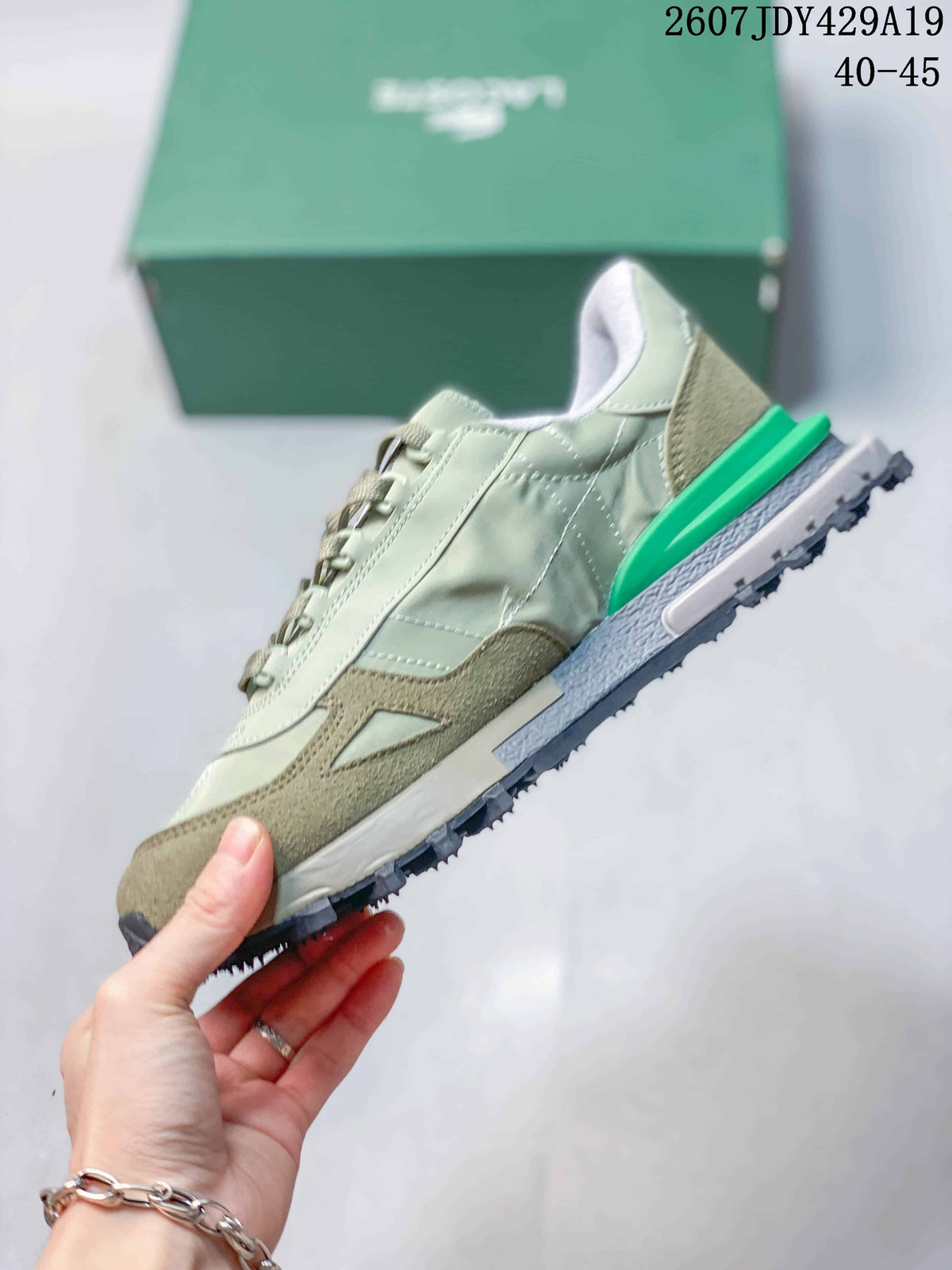 Side view of a pale green and khaki Lacoste sneaker with lace-up construction and a contrasting green heel piece.