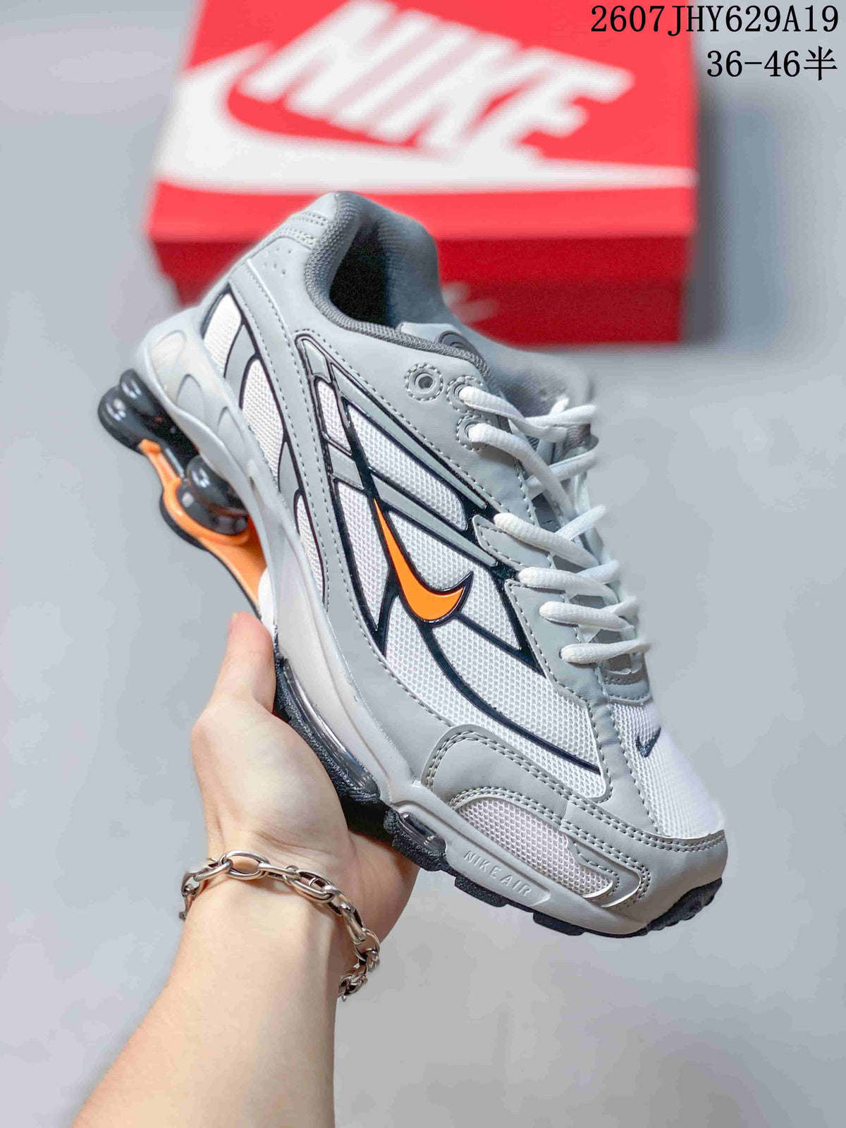 Angled side view showing the grey and white upper, orange Swoosh detail, black outsole and visible heel columns.
