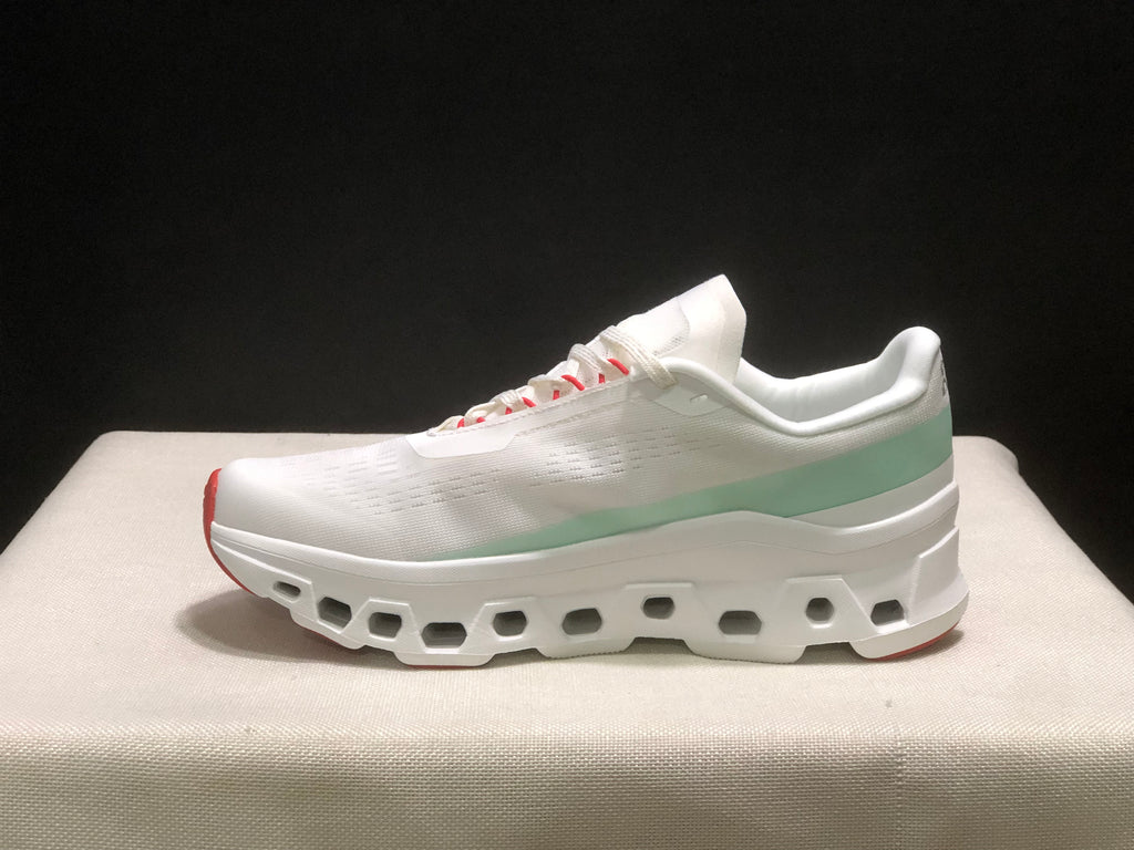 Full side profile of one white On Cloudmonster 1 sneaker with pale green heel detail and a segmented outsole.