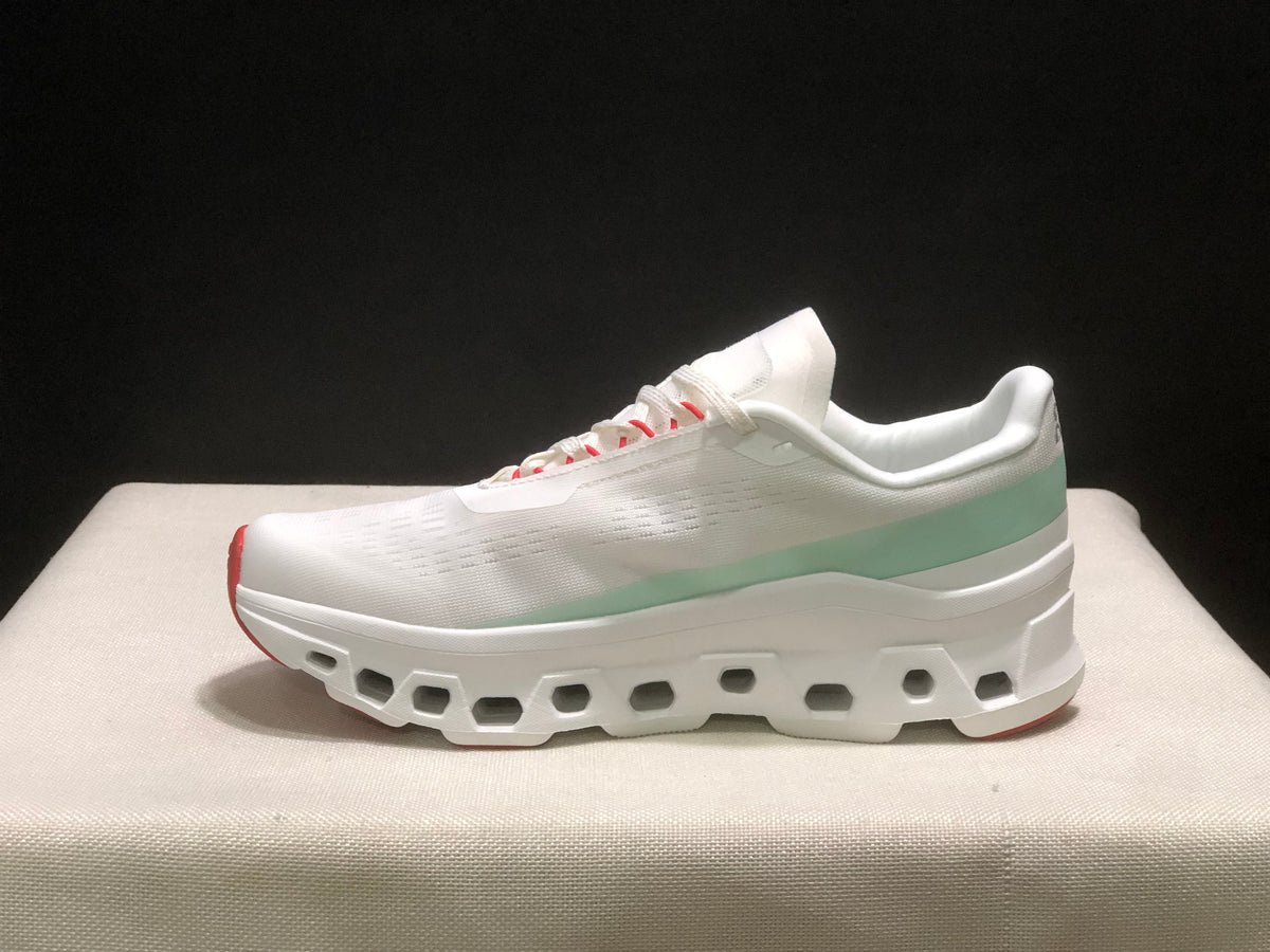 Full side profile of one white On Cloudmonster 1 sneaker with pale green heel detail and a segmented outsole.