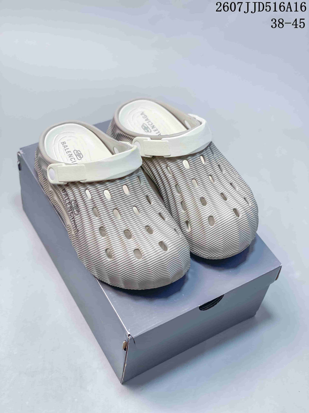 Pair of light beige closed-toe clogs displayed on a shoe box, showing the wave-textured upper, ventilation openings, and heel straps.