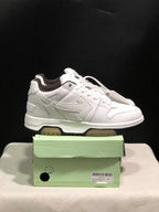 Side view of a white sneaker pair on a shoe box, highlighting the layered tonal panels and contrast outsole.