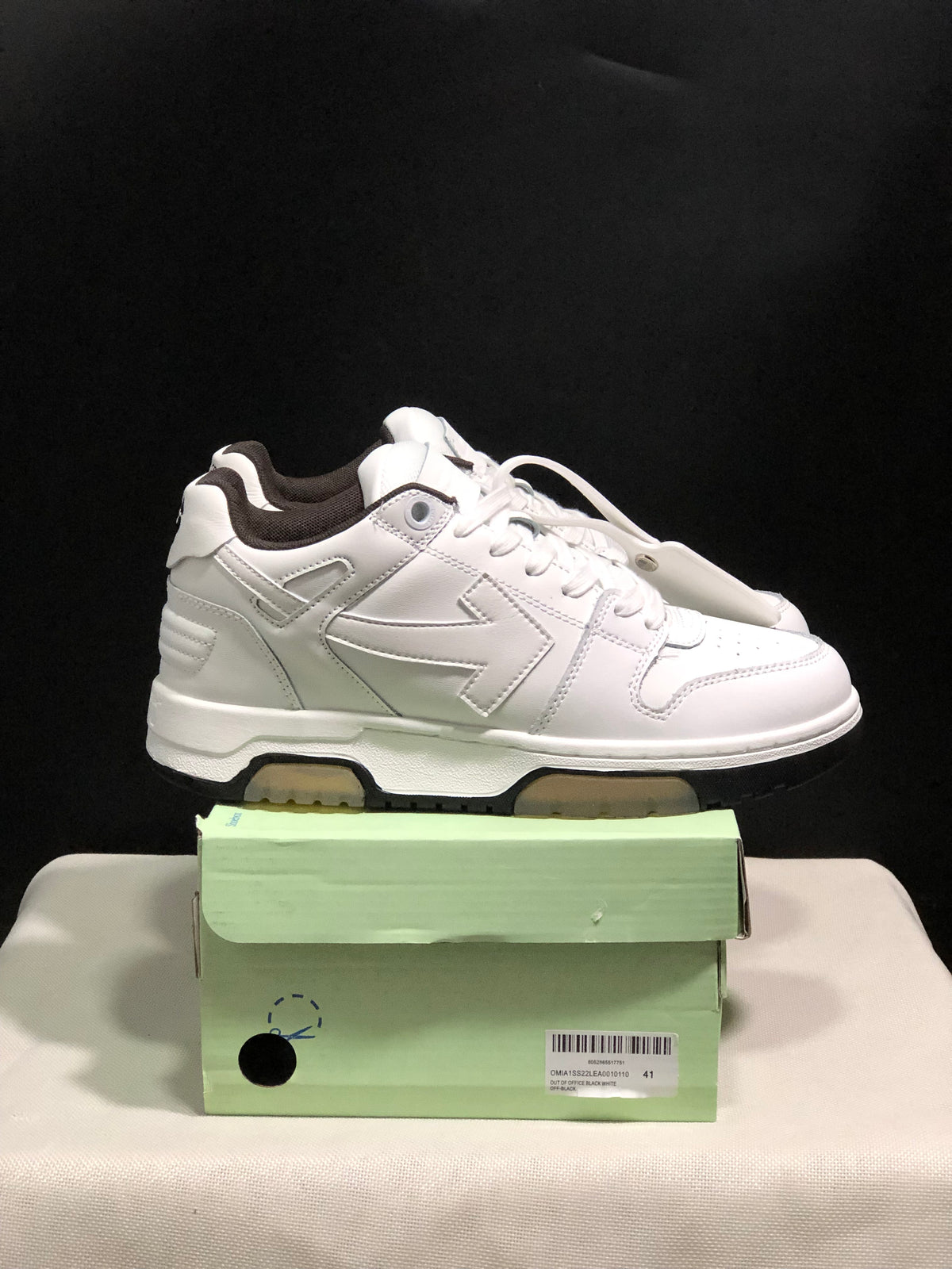 Side view of a white sneaker pair on a shoe box, highlighting the layered tonal panels and contrast outsole.