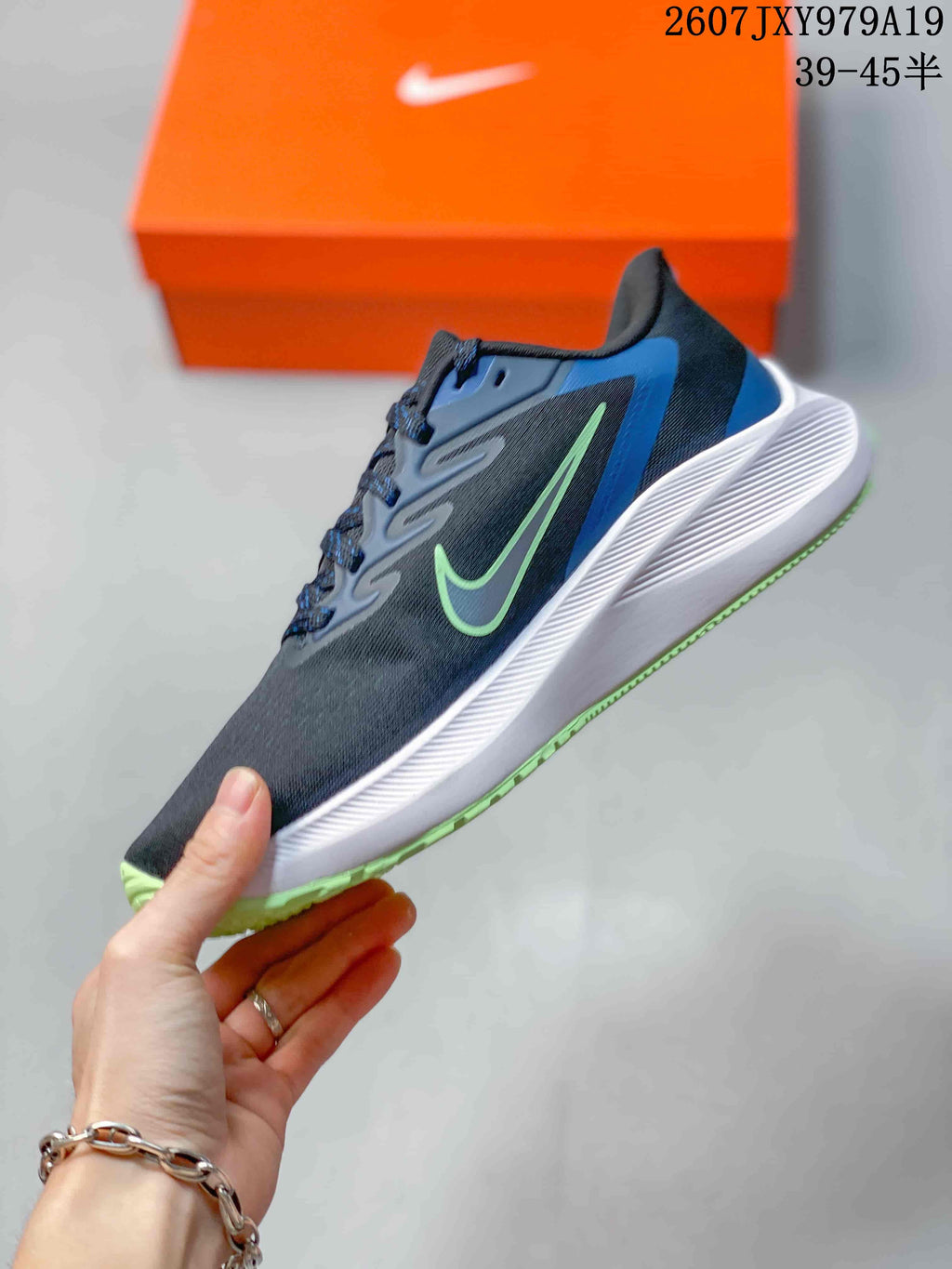 Side view of the low-top sneaker showing the dark upper, green side logo, blue heel panel, white midsole, and green outsole edge; overlay shows style code 2607JXY979A19 and size range 39–45.