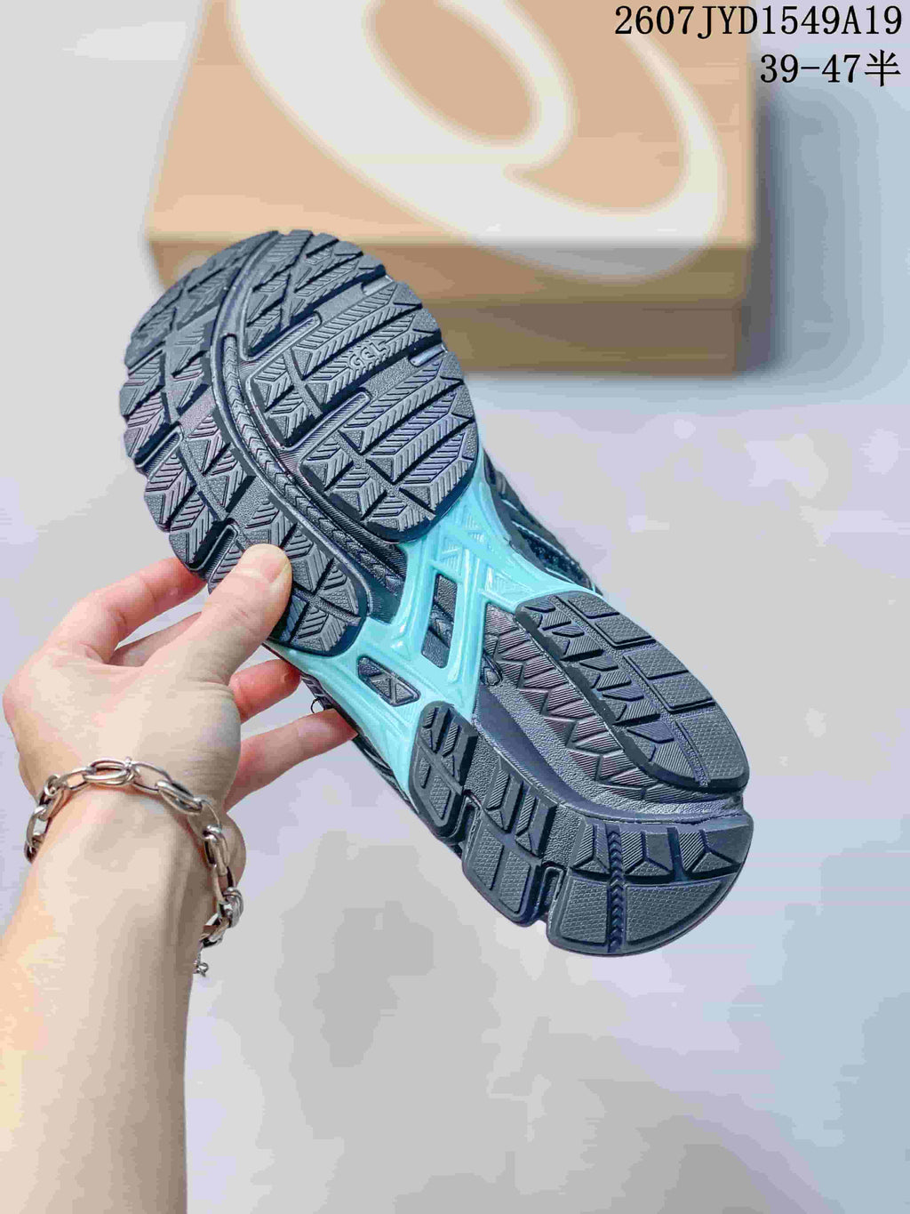 Underside view of an ASICS sneaker showing the segmented patterned rubber outsole and light aqua midsole detail; image text shows style code 2607JYD1549A19 and size range 39–47.5.