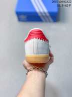Rear view of the white sneaker showing red heel detailing, visible stitching, and the gum-colored outsole.