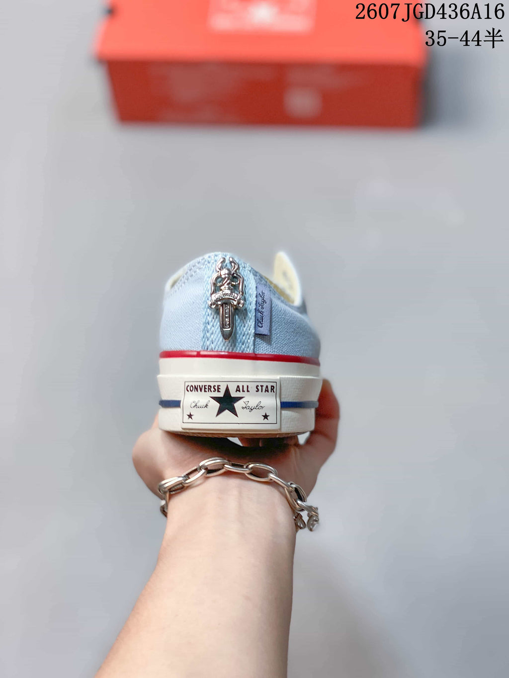 Rear view of a light blue sneaker showing the Converse All Star heel patch, red and blue sole stripes, and a decorative heel detail.