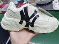 Beige chunky sneaker with a dark NY logo, layered panels, white laces, and a textured sole held in hand.