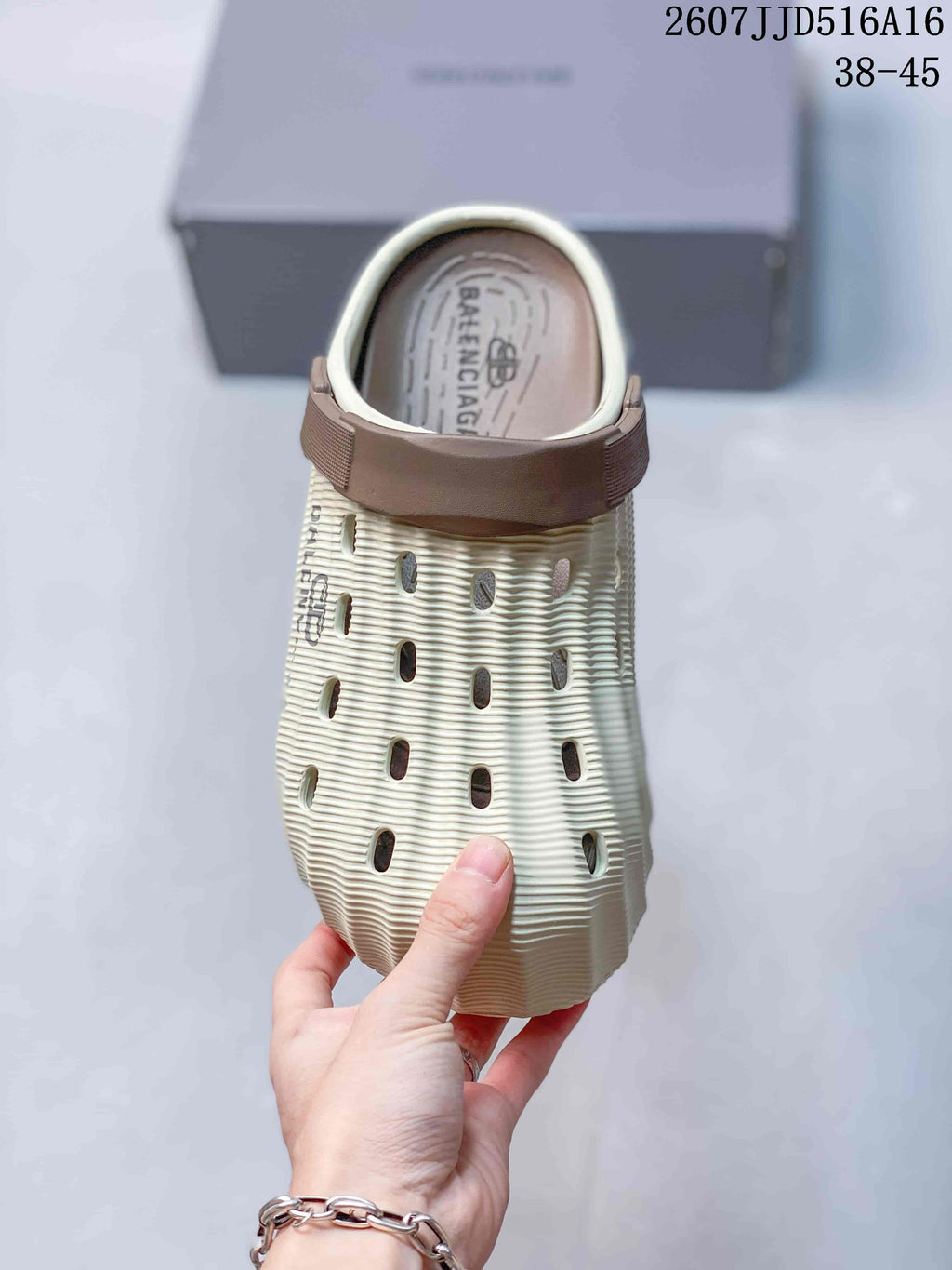 Top view of a cream clog slide with brown heel strap, ventilation openings, ribbed texture, and Balenciaga branding on the footbed.