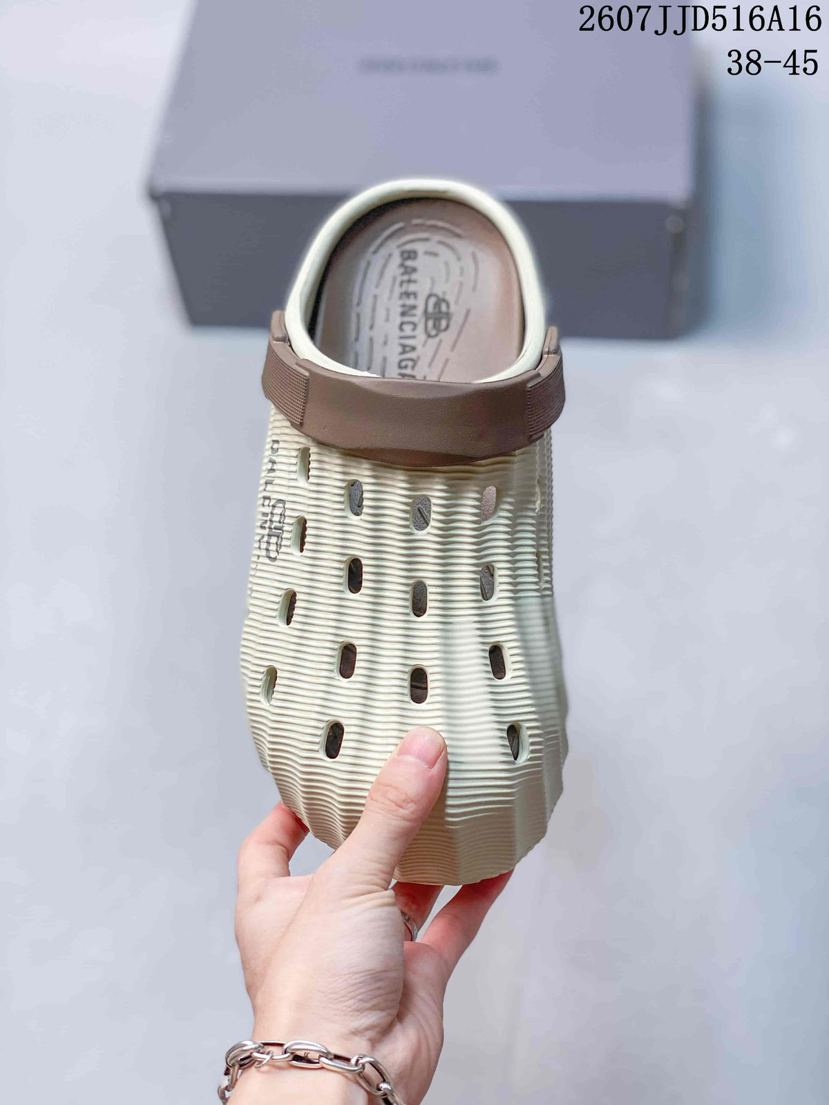 Top view of a cream clog slide with brown heel strap, ventilation openings, ribbed texture, and Balenciaga branding on the footbed.