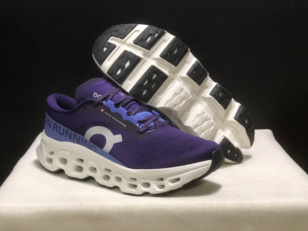 Angled view of the purple shoes with one outsole lifted to show the black tread sections and white midsole structure.
