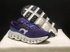 Angled view of the purple shoes with one outsole lifted to show the black tread sections and white midsole structure.
