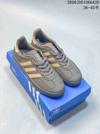 Pair of gray Adidas Originals Gazelle sneakers with gold-toned stripes and heel accents, displayed on a blue Adidas shoebox.