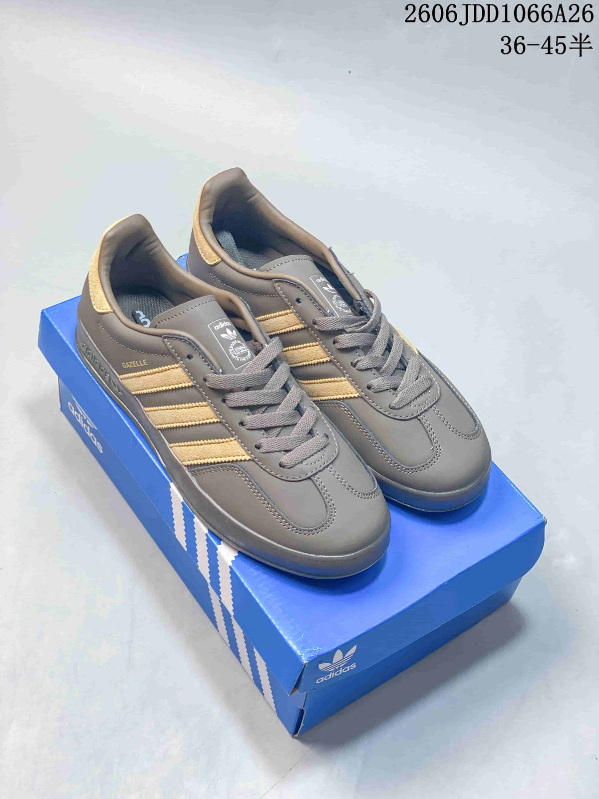 Pair of gray Adidas Originals Gazelle sneakers with gold-toned stripes and heel accents, displayed on a blue Adidas shoebox.