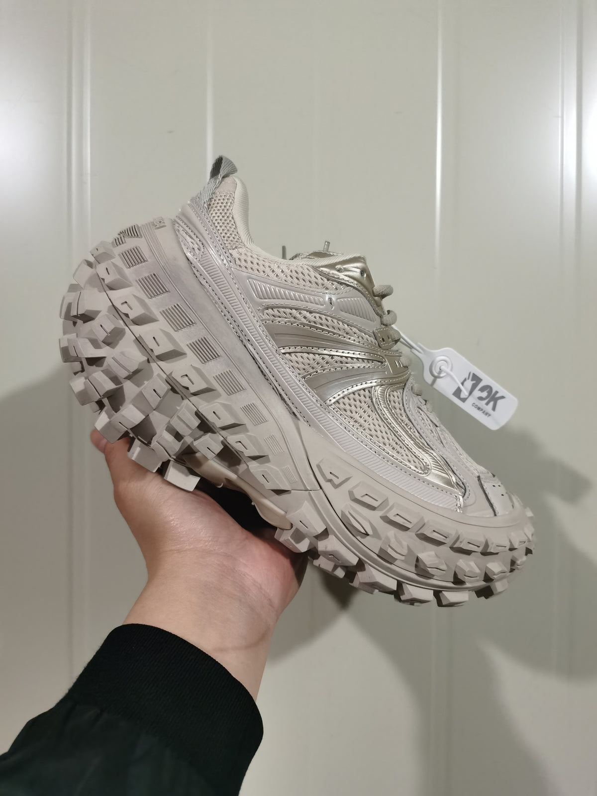 Three-quarter front view of a beige sneaker with a rounded toe, lace-up closure, and deep rubber outsole tread.