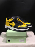 Pair of black and yellow low-top sneakers displayed on a green shoe box, showing the front and outer side.