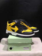 Pair of black and yellow low-top sneakers displayed on a green shoe box, showing the front and outer side.