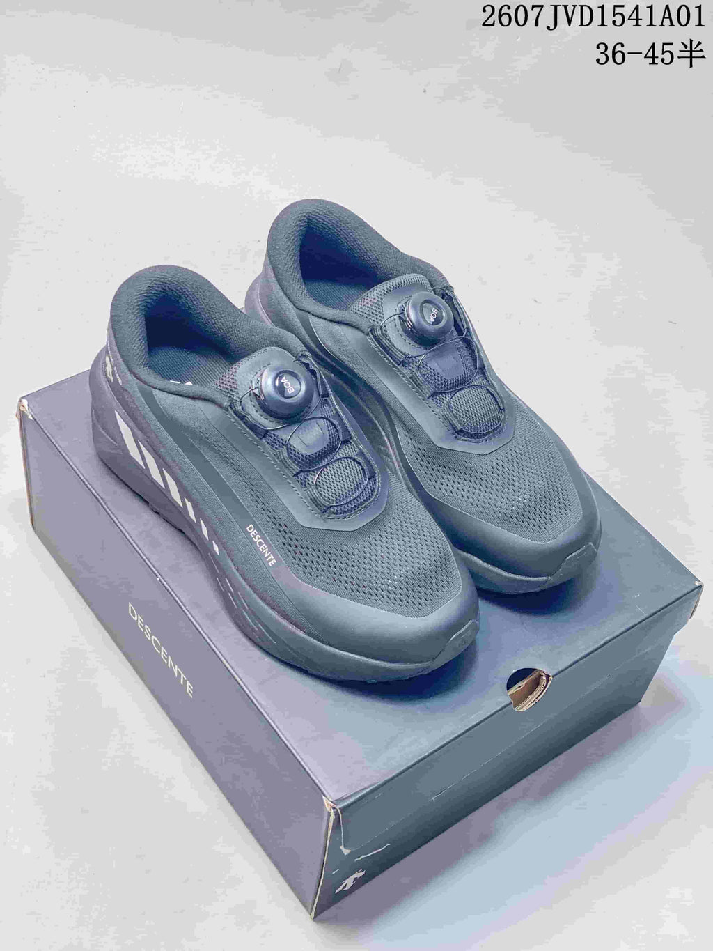Dark gray Descente low-top running shoes with dial closures, displayed on a box.